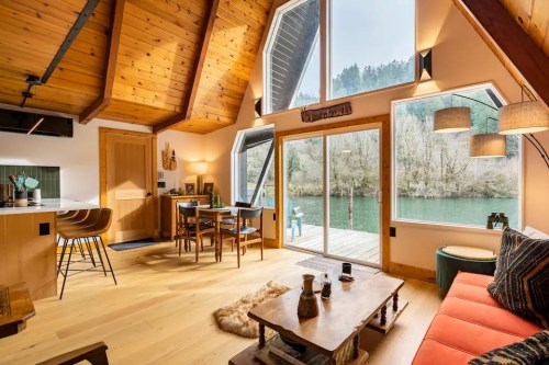 Cozy cabin interior with wooden beams, a river view, and a mix of modern and rustic furniture.