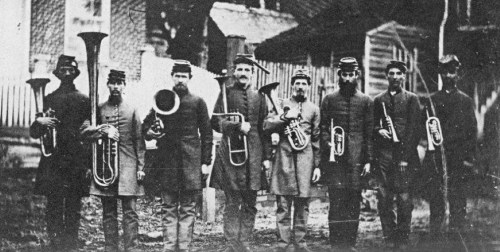 A historical black-and-white photo of nine men in military uniforms holding brass instruments.