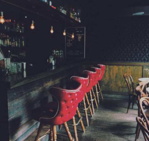 Cozy bar interior featuring red upholstered stools, wooden counter, and dim lighting.