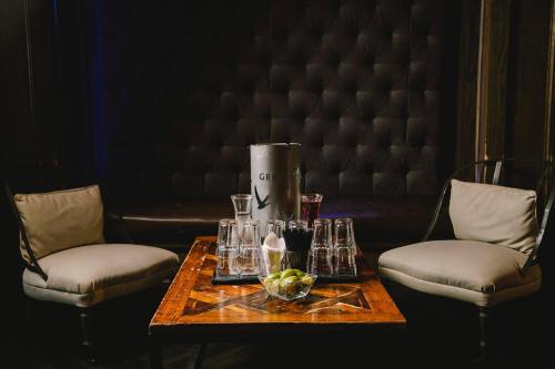 A cozy lounge setting with two chairs, a wooden table, and a bottle of Grey Goose surrounded by glasses and garnishes.
