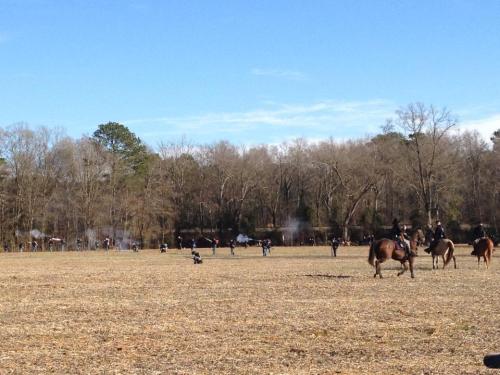 A wide field with people on horseback and smoke in the background, suggesting a historical reenactment or event.