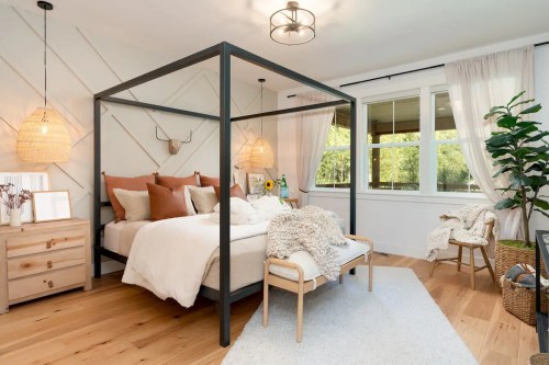 Cozy bedroom featuring a four-poster bed, warm decor, wooden furniture, and large windows with natural light.