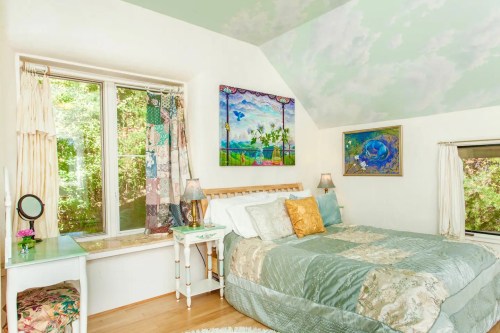 Cozy bedroom with a bed, colorful artwork, and large windows letting in natural light.