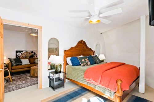 Cozy bedroom with a wooden bed, colorful bedding, and a sitting area featuring a sofa and decorative accents.