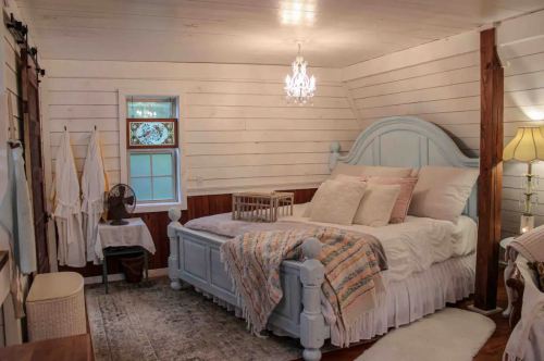 Cozy bedroom with a light blue bed, soft bedding, a chandelier, and warm wooden accents. Natural light from a window.