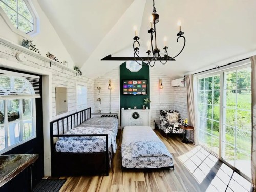 Cozy room with two beds, a chandelier, and large windows, featuring a green accent wall and a TV.