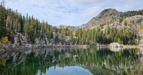A calm lake reflects the trees and mountains at one of the best hiking trail near Brighton Resort Utah.