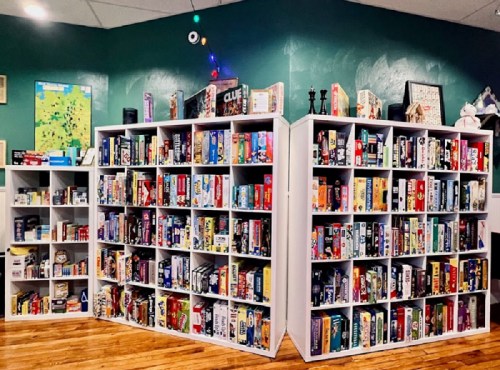 A cozy game room with two white bookshelves filled with various board games against a green wall.
