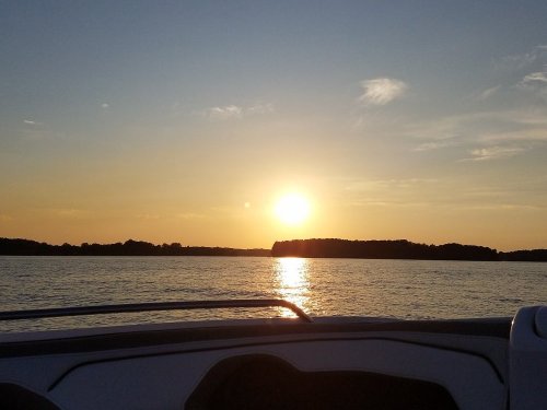 A serene sunset over a calm lake, with silhouettes of trees on the horizon and gentle ripples on the water.
