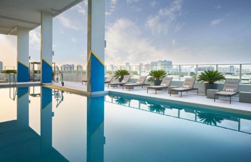 Rooftop pool with lounge chairs and city skyline in the background under a clear blue sky.