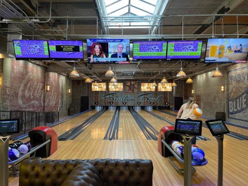 A bowling alley with multiple screens showing news and scores, featuring wooden lanes and a cozy seating area.