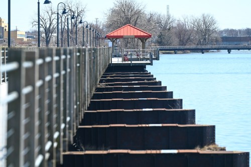 A wooden pier extends into a calm body of water, featuring a red-roofed gazebo and lined with lampposts.