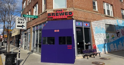 A coffee shop with a purple vestibule is located on a street corner with colorful murals nearby.
