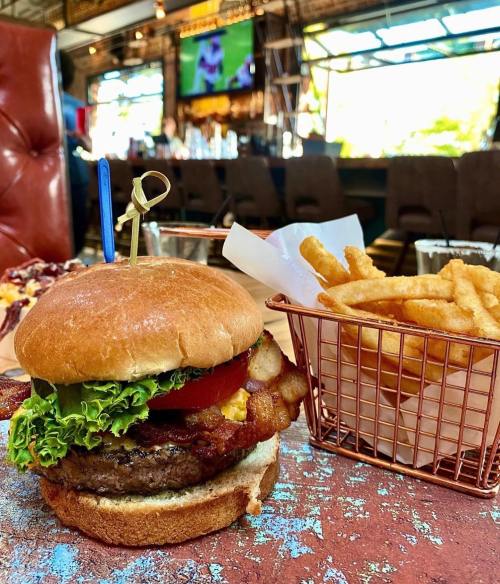 A juicy burger with lettuce, tomato, and bacon, served with a side of crispy fries in a basket.