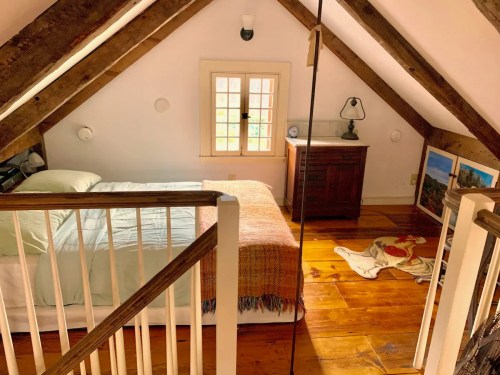 Cozy attic bedroom with a bed, wooden furniture, and sloped ceilings, featuring warm wood floors and natural light.