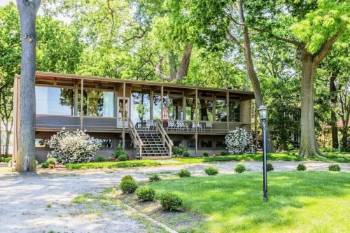 A modern house with a large porch, surrounded by greenery and trees, set in a well-maintained yard.