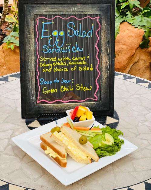A chalkboard menu displays an egg salad sandwich with sides, alongside a plate featuring the sandwich and fresh vegetables.