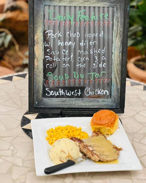 A chalkboard menu displays daily features, including pork chop, mashed potatoes, corn, and a roll on a table.