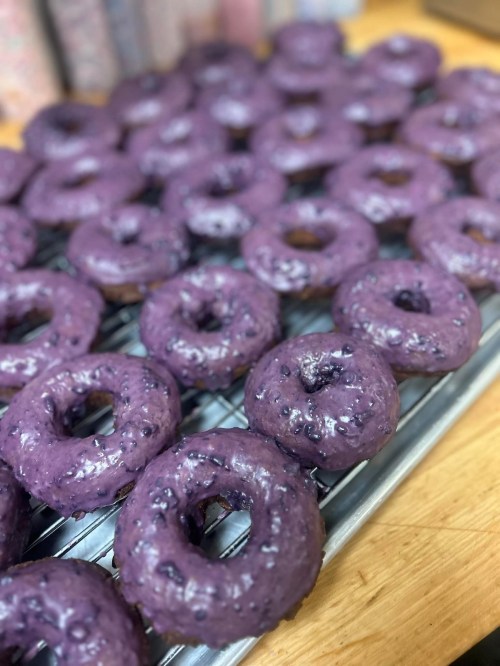 A tray of freshly baked purple donuts cooling on a wire rack.