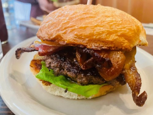 A juicy burger with bacon, cheese, and lettuce on a toasted bun, served on a white plate.