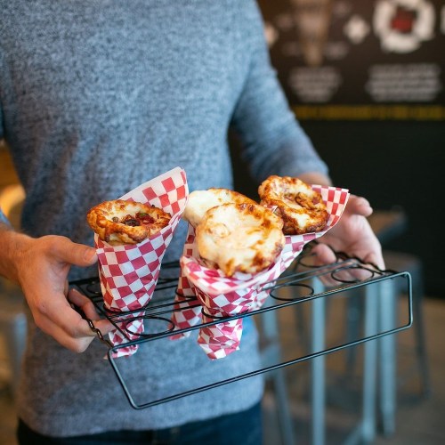 A person holds a tray with three food cones wrapped in red and white checkered paper.