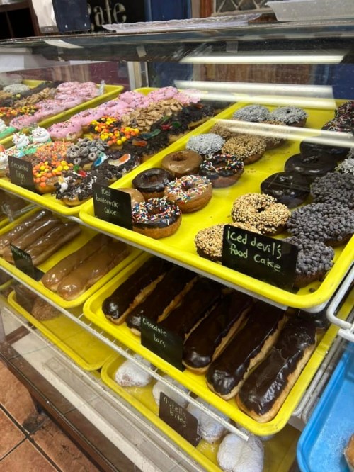 A display case filled with colorful donuts, chocolate bars, and cakes, showcasing a variety of sweet treats.