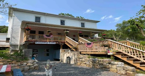 A two-story white building with a wooden deck, featuring flower pots and patriotic decorations, labeled "Country Cafe."