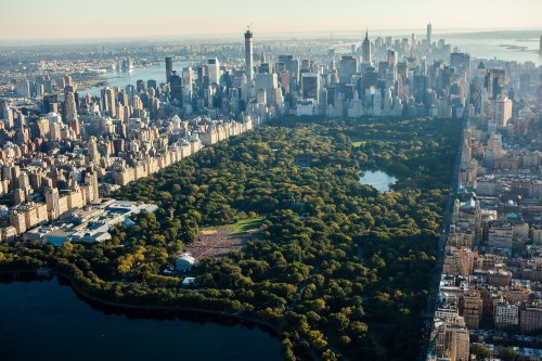 Aerial view of Central Park surrounded by skyscrapers in New York City, showcasing lush greenery and water features.