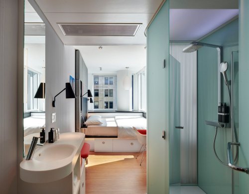 Modern hotel room featuring a bed, sleek bathroom with shower, and large windows for natural light.