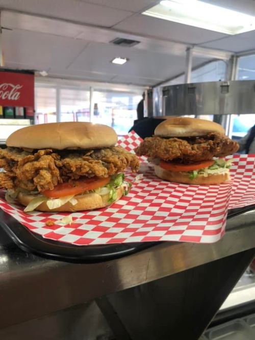 Two fried chicken sandwiches on a tray, topped with lettuce and tomato, served in red and white checkered paper.