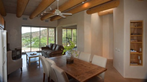 Modern interior featuring a dining area, living space, and large windows with a view of nature. Warm, earthy tones.