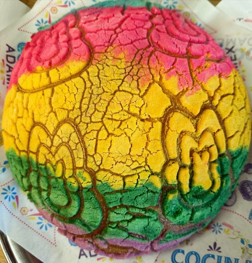 A colorful pan dulce with a vibrant pink, yellow, and green design, featuring floral patterns on top.