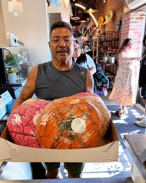 A man holds a box with large, colorful round items while standing in a vibrant shop.