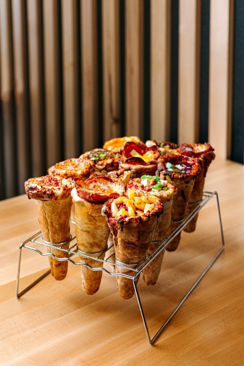 A display of pizza cones on a metal rack, featuring various toppings, set on a wooden table.