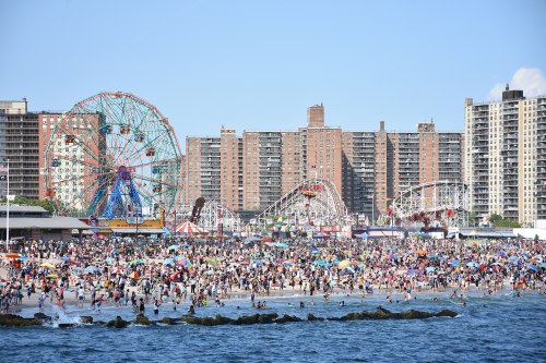 A crowded beach scene with amusement rides in the background and people enjoying the sun and water.