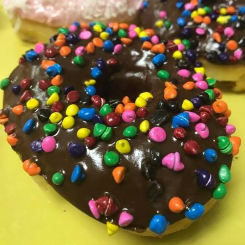 A chocolate donut topped with colorful sprinkles on a yellow background.