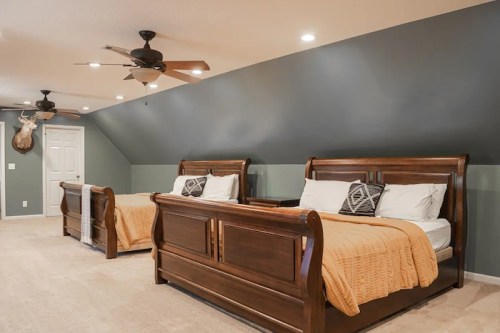 A spacious bedroom with two wooden sleigh beds, orange blankets, and a sloped ceiling with ceiling fans.