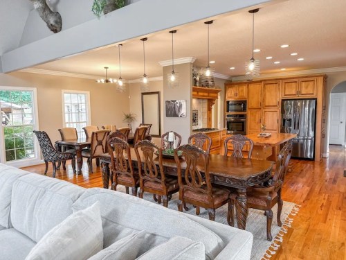 A spacious dining area with a large wooden table, elegant chairs, and a modern kitchen in the background.