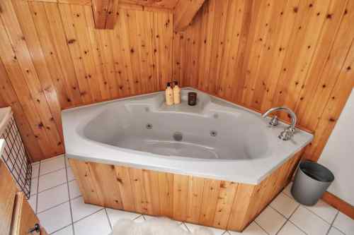 A corner jacuzzi tub in a wooden-paneled bathroom, with toiletries and a small trash can nearby.