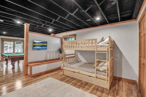 A cozy room featuring a wooden bunk bed, a TV on the wall, and a pool table in a well-lit space with wooden flooring.