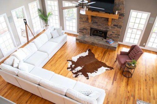 Spacious living room with a large white sectional, a brown cowhide rug, a pink chair, and a stone fireplace.