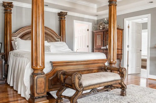 Elegant bedroom featuring a four-poster bed, wooden columns, and a decorative bench in a warm, inviting setting.
