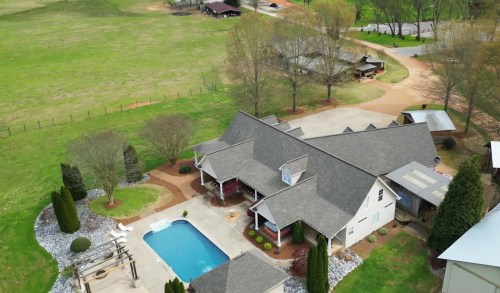 Aerial view of a spacious home with a pool, surrounded by greenery and outbuildings on a rural property.
