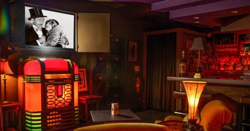 Interior of a SoCal speakeasy known as the Rendition Room, showing warmly lit interior with lots of cozy seating and vintage film playing