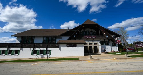 Exterior view of Turner Hall, a large building with a sloped roof, featuring flags and a bowling sign under a blue sky.
