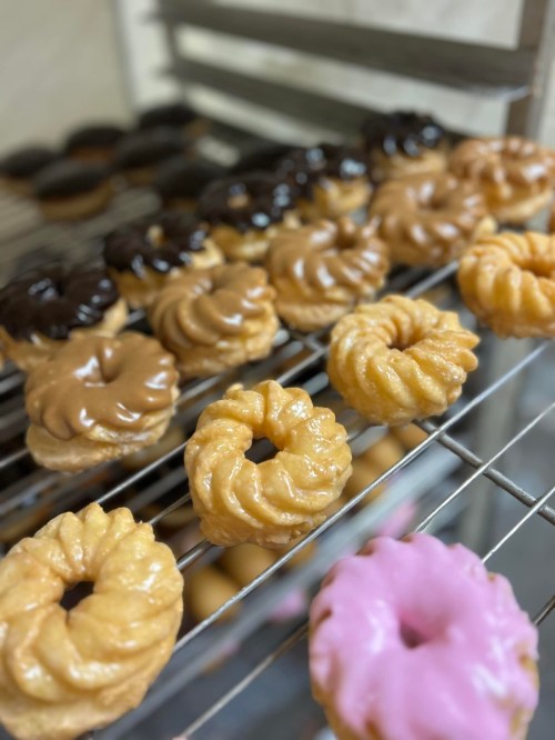 A variety of freshly made donuts on a cooling rack, featuring chocolate, caramel, and pink icing.