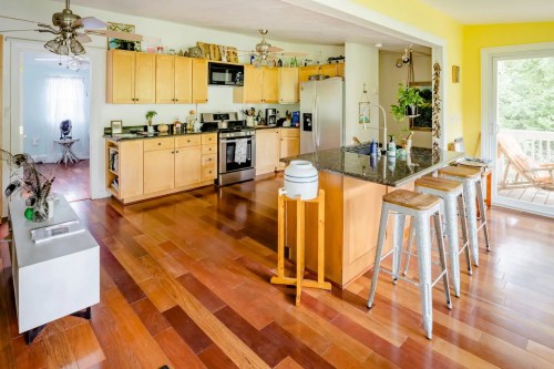 Bright kitchen with wooden cabinets, granite island, and bar stools, featuring an open layout and natural light.
