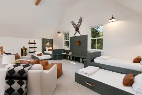 A cozy, modern bedroom with two beds, a seating area, and natural light from large windows. Decor includes wall art.