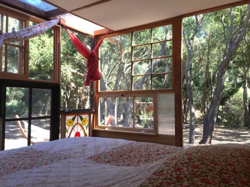 Cozy bedroom with a quilt, large windows, and a view of trees outside, creating a serene, natural atmosphere.