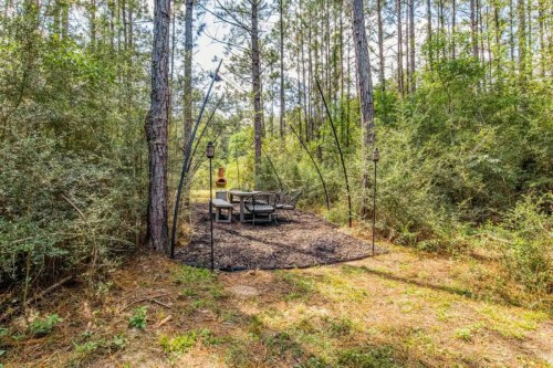 A secluded outdoor dining area surrounded by tall trees and greenery, featuring a table and chairs on a gravel path.